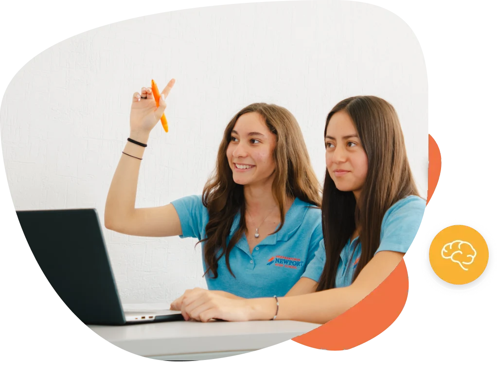Dos alumnas de Newport High School participando en clase, una levanta la mano con una pluma